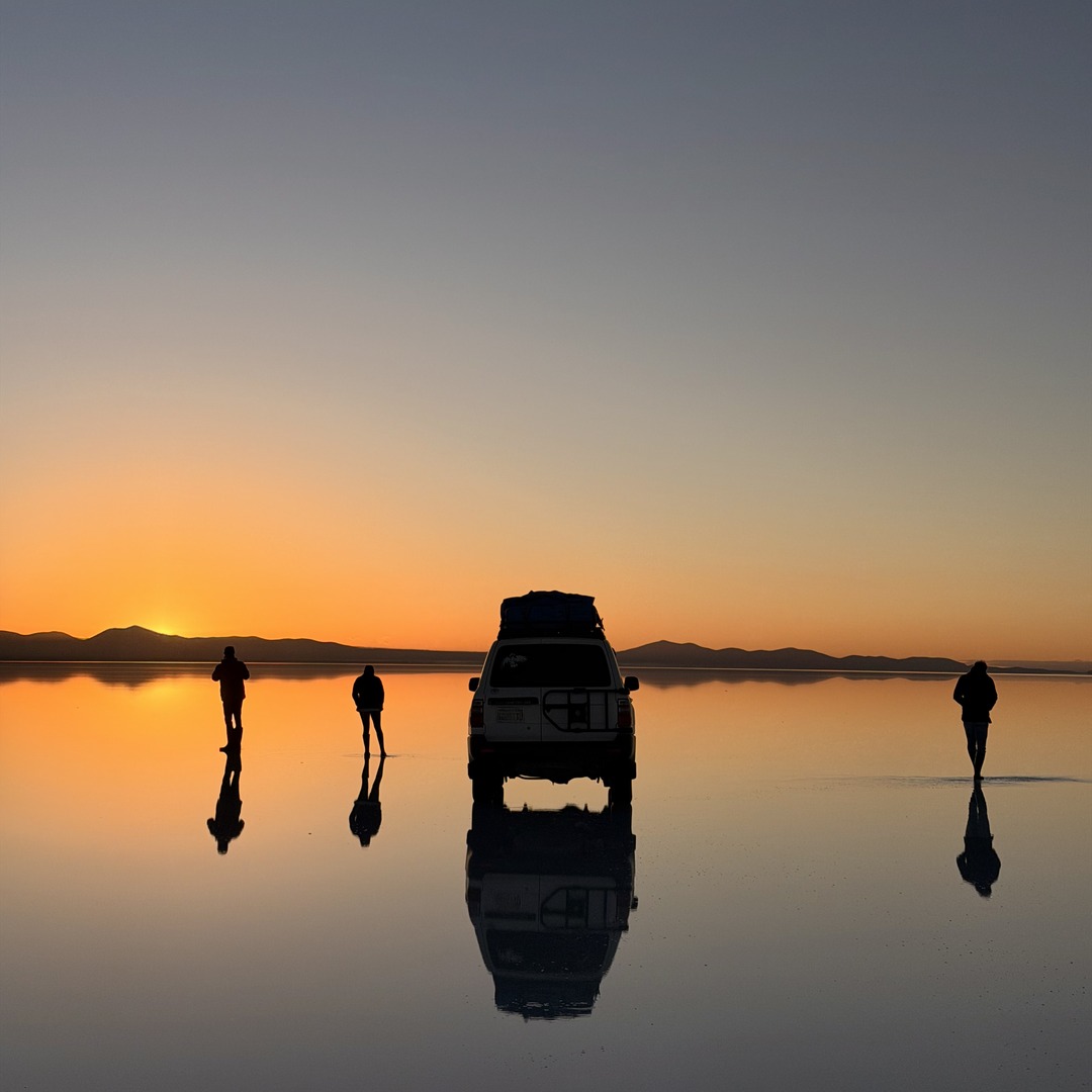 Our group and four-wheel drive reflected on the Uyuni salt flats at sunrise