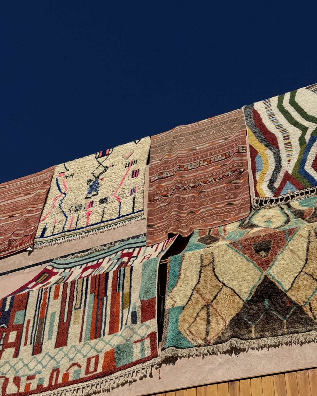 Handwoven Berber rugs hanging on a wall against a deep blue sky in Marrakech, Morocco