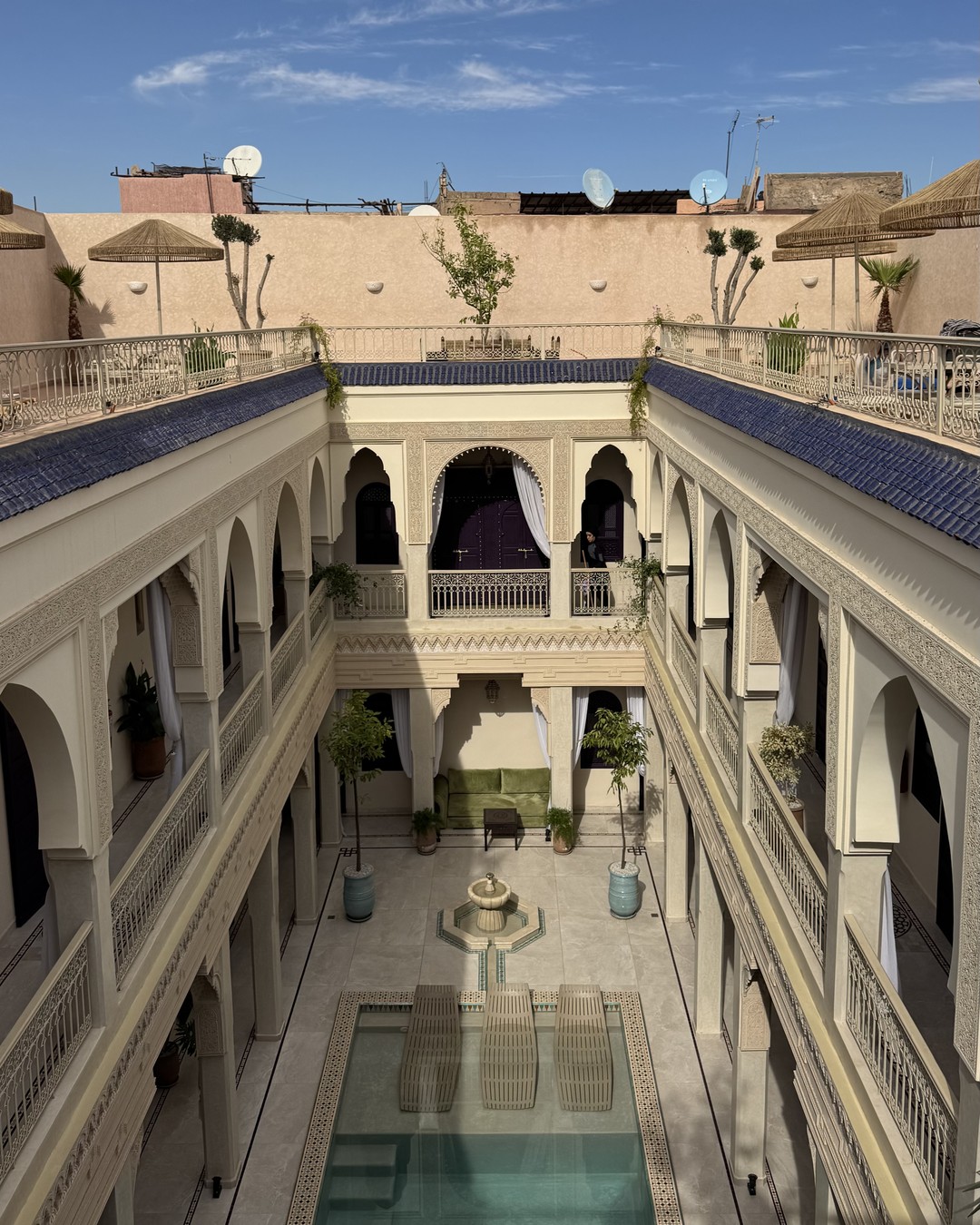 Riad courtyard in daylight with a fountain, orange trees and arched galleries in Marrakech, Morocco