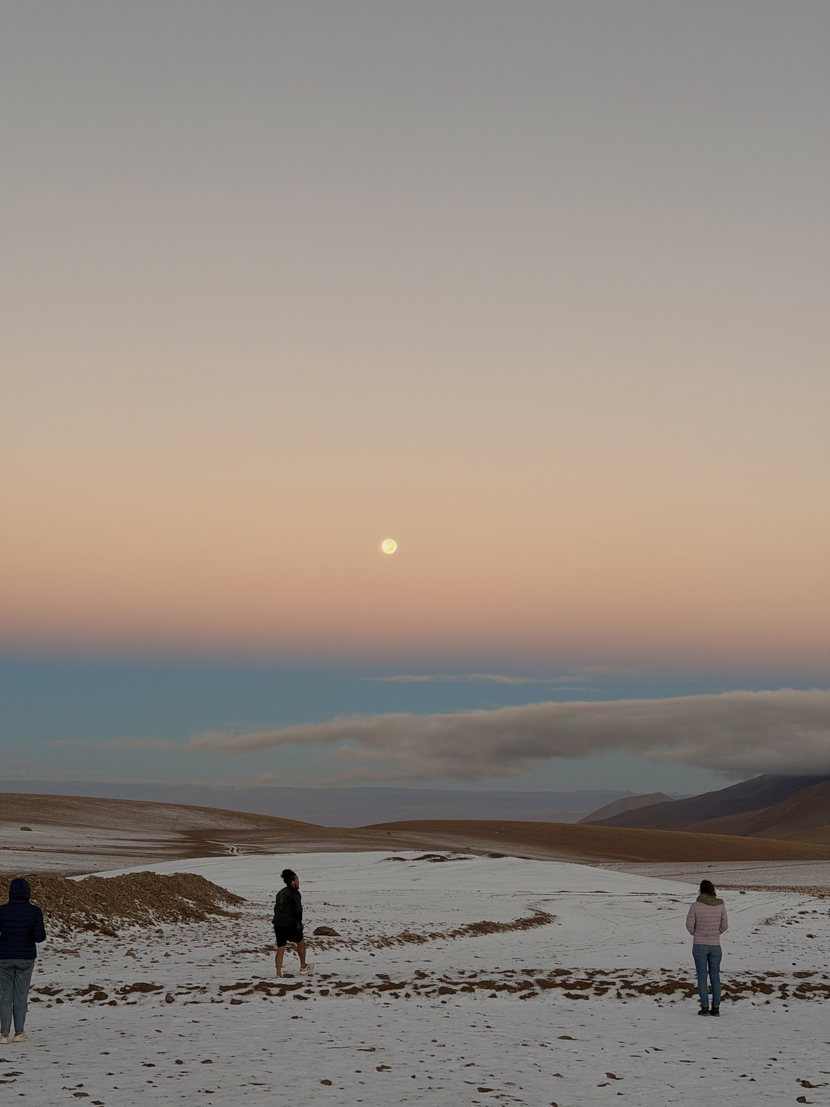 Travellers standing on snowy ground near the Chile to Bolivia border at dawn