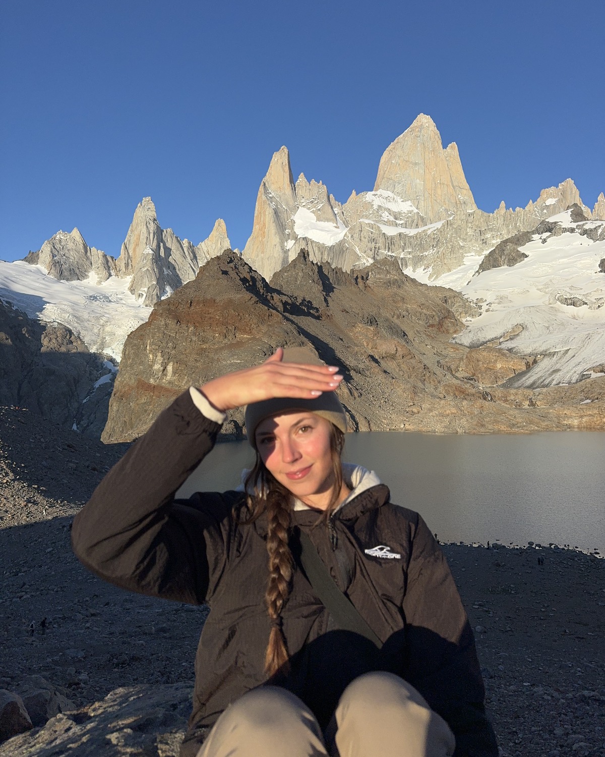 Ellen wearing warm layers beside Laguna de los Tres with the Fitz Roy peaks behind her