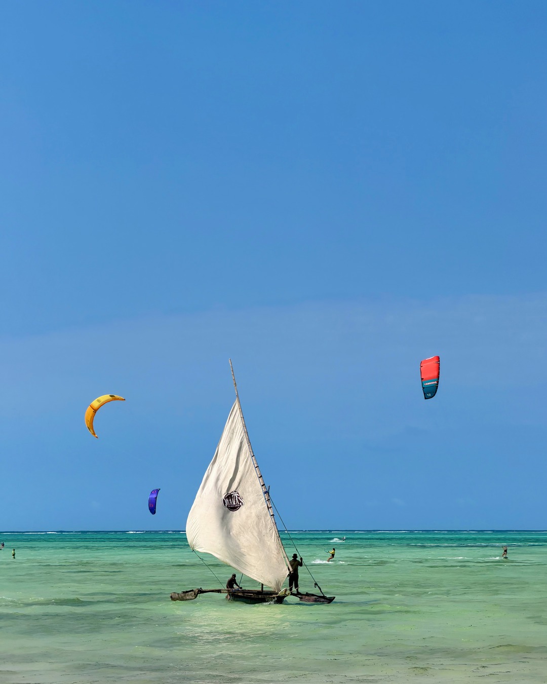 A traditional sailing boat and colourful kites over the turquoise water at Paje beach
