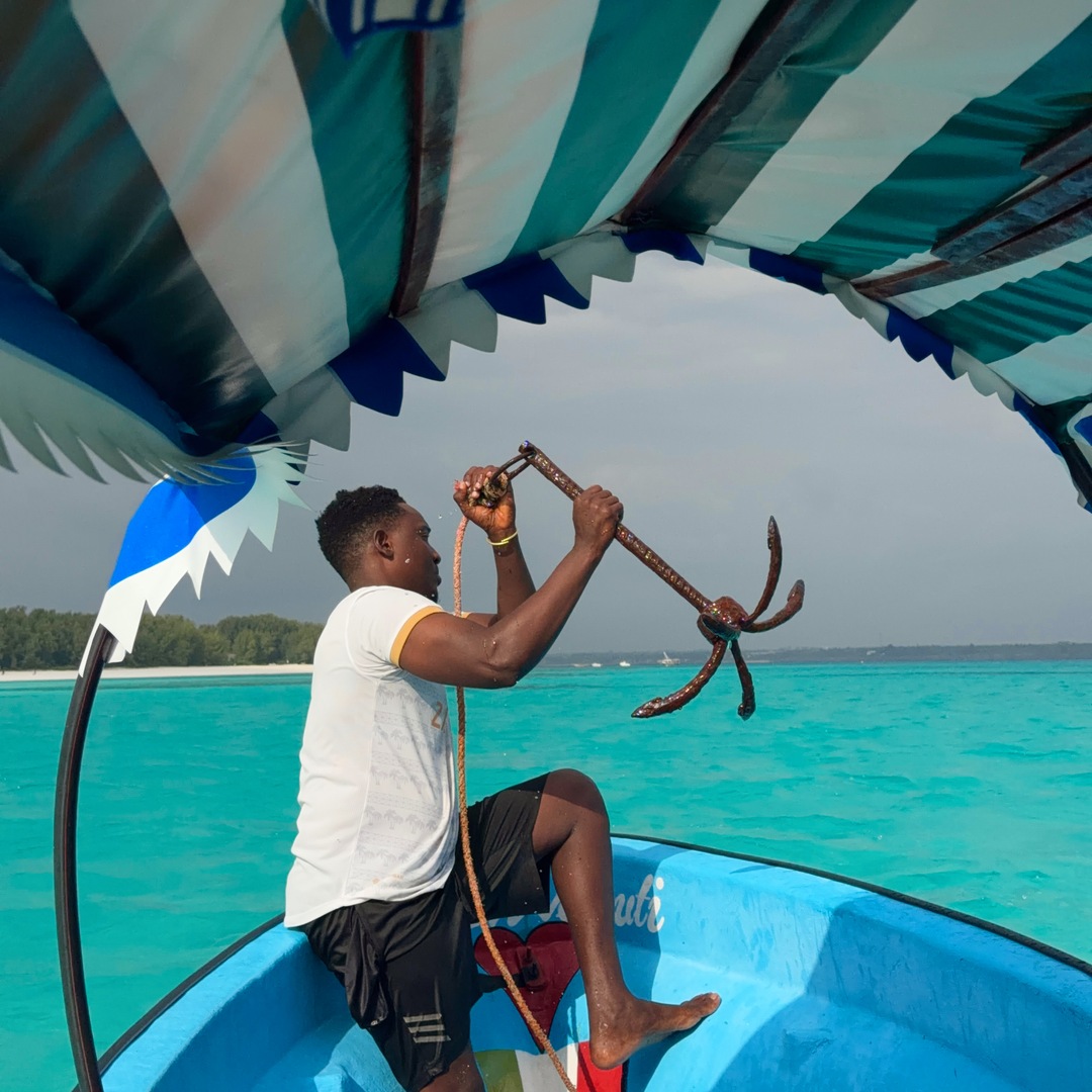 Our boat guide lifting the anchor above turquoise water near Mnemba, Zanzibar