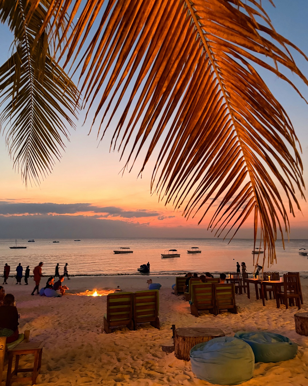 Palm fronds over boats and sunset beach seating at Bobo in Nungwi, Zanzibar